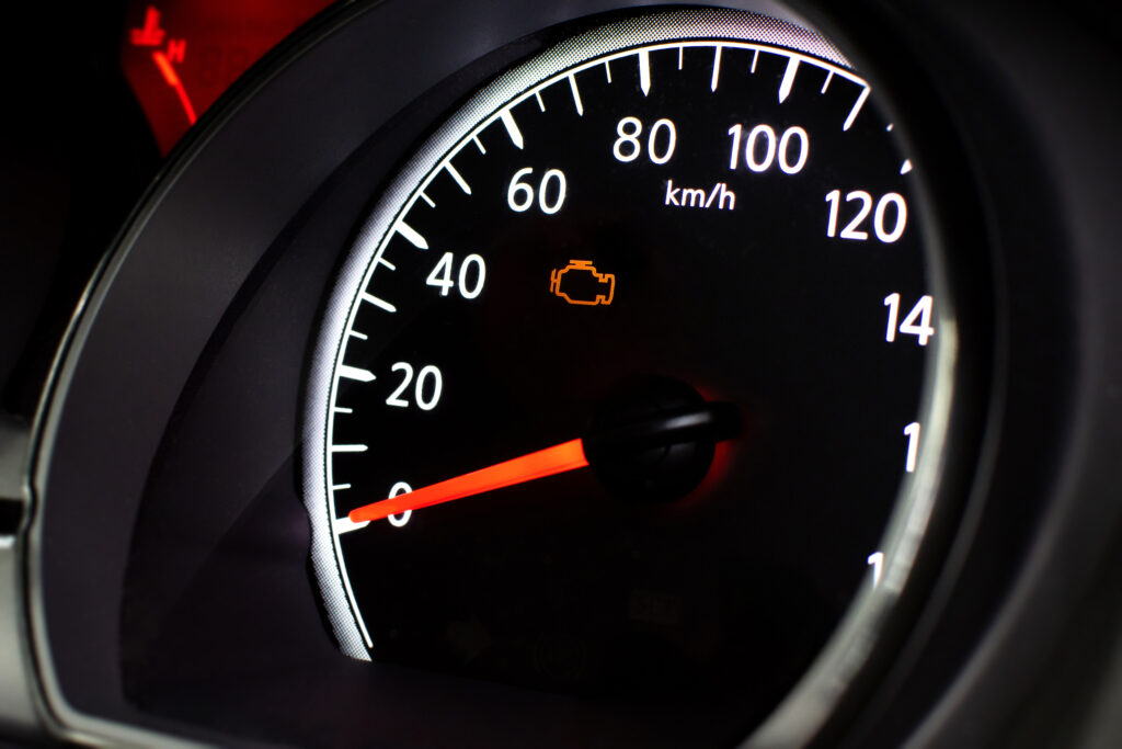 A car speedometer with an illuminated orange check engine light.