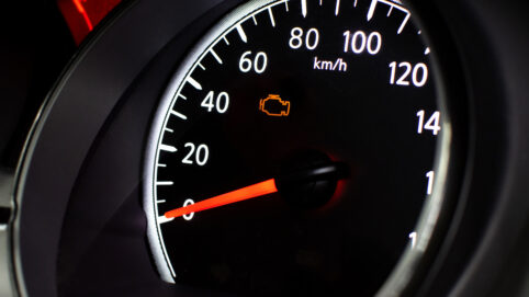 A car speedometer with an illuminated orange check engine light.