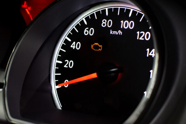 A car speedometer with an illuminated orange check engine light.
