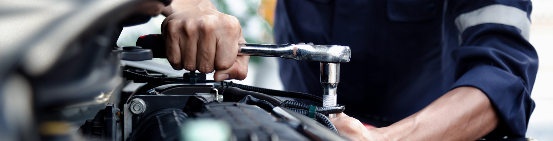 A mechanic using a wrench to repair and maintain an auto engine at an auto repair shop.