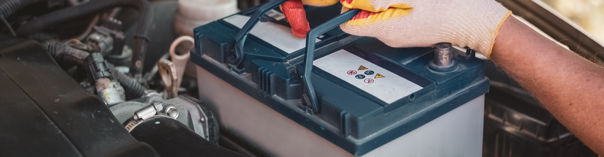 An auto mechanic removing a BMW’s battery under the hood of the car.