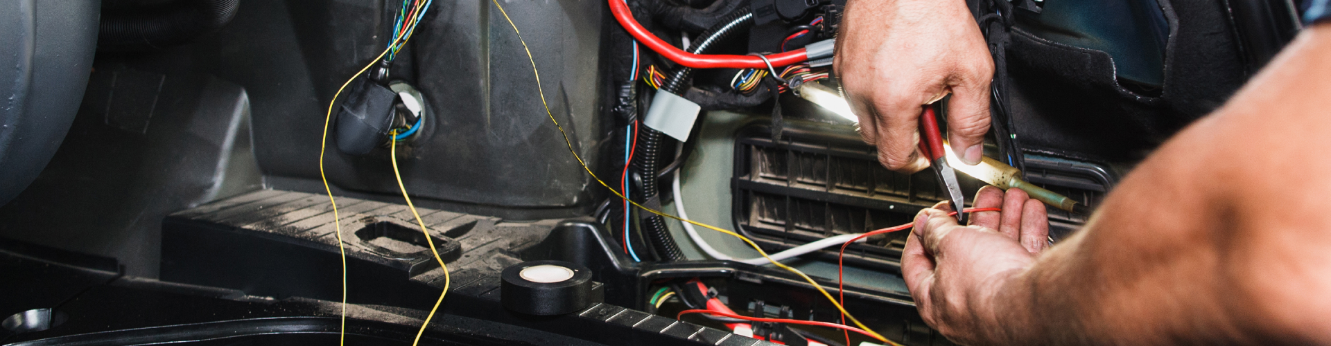 Close-up of a BMW’s electrical panel inside the trunk with an auto mechanic working on repair and module coding.