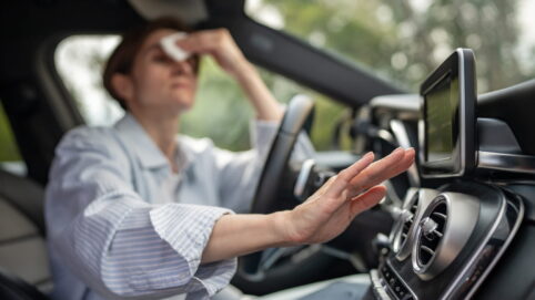Woman drives car with broken air conditioning in hot Woodinville, WA, summer weather. Wipes sweat paper napkin.