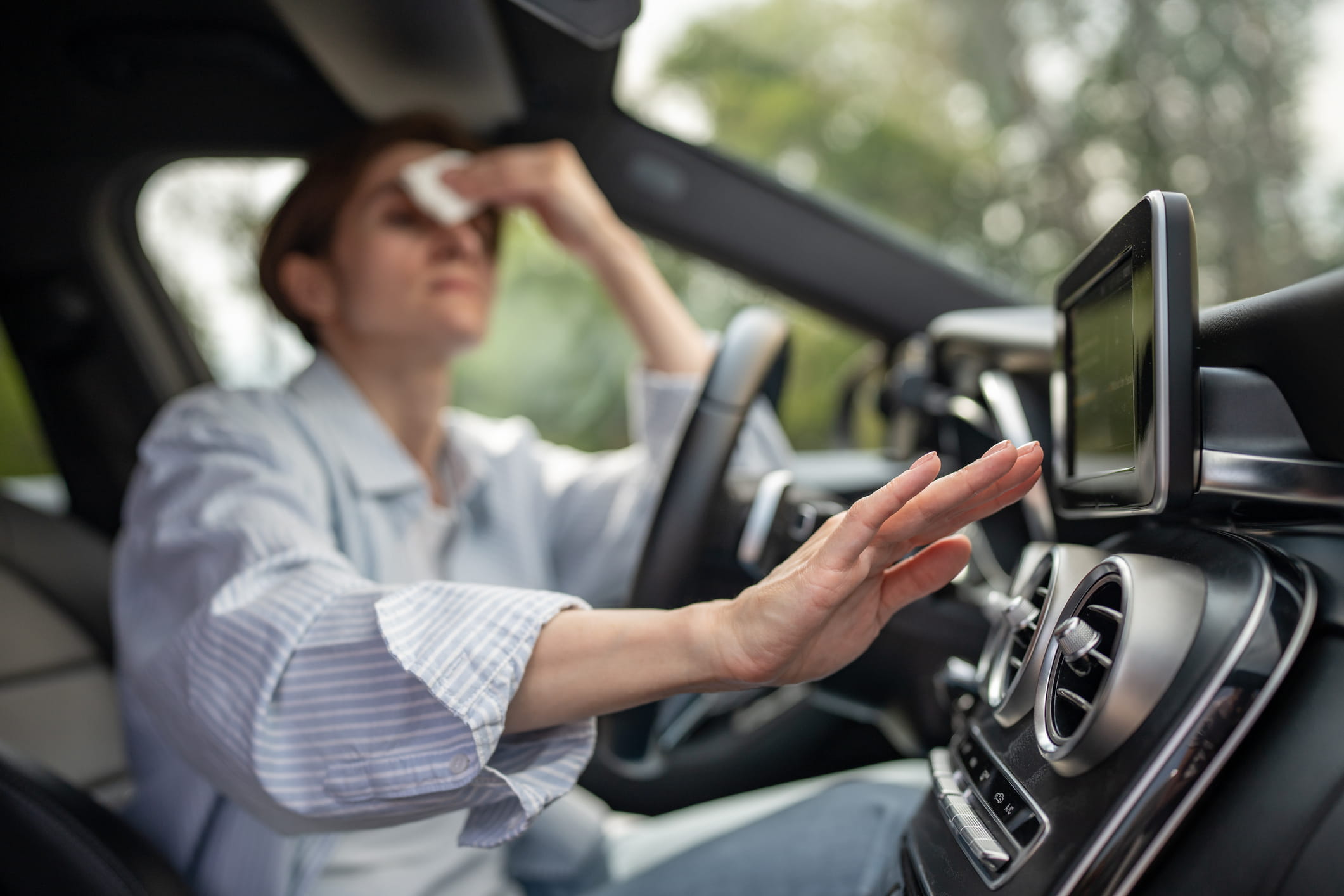 Woman drives car with broken air conditioning in hot Woodinville, WA, summer weather. Wipes sweat paper napkin.