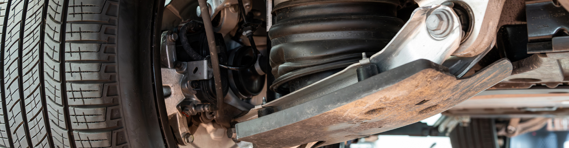 Wide-angle of a BMW’s rear axle assembly with control arm and air suspension shock absorber with rubber boot.