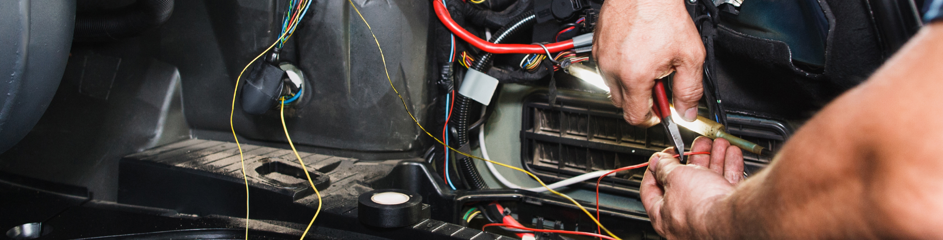 Mechanic performs electrical repairs for Audi vehicle, using their hands and a tool.