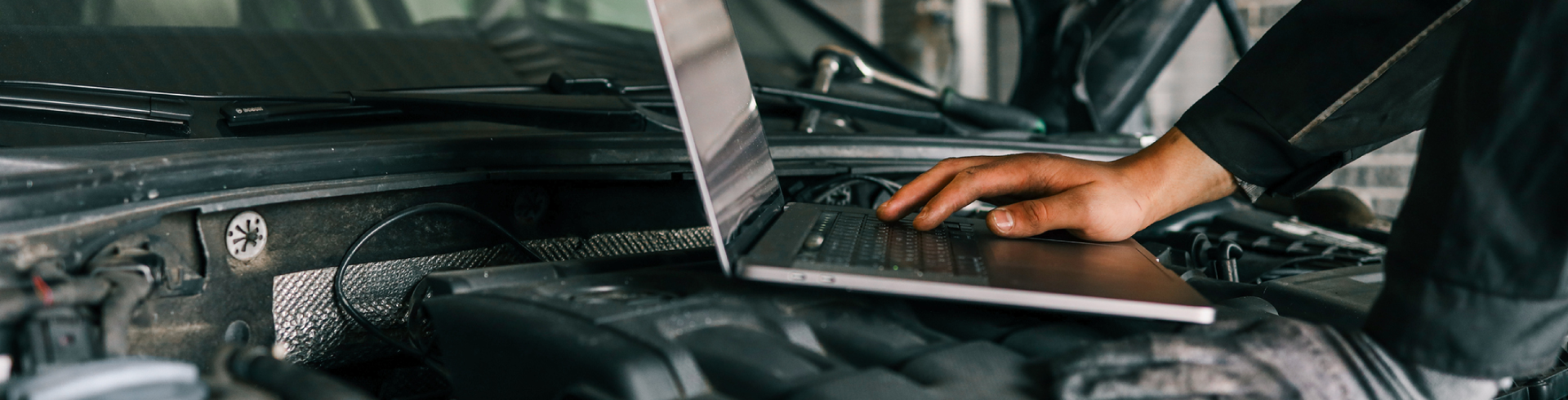A mechanic using a laptop on a car engine for diagnostics in a garage. Performing routine maintenance for Audi.