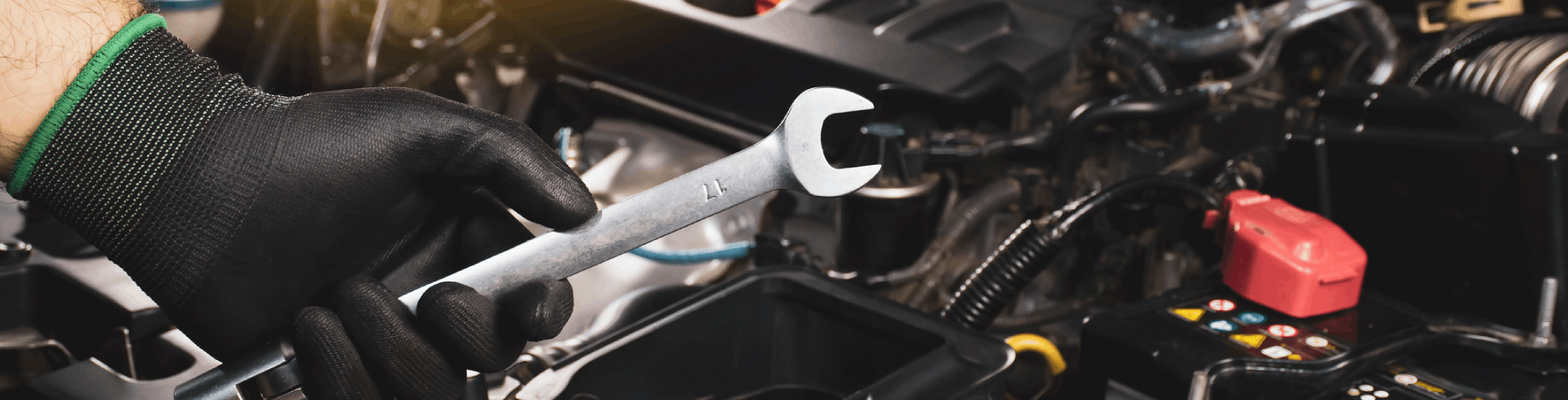 Mechanic wearing black gloves uses a wrench to repair MINI Cooper engine in auto shop.