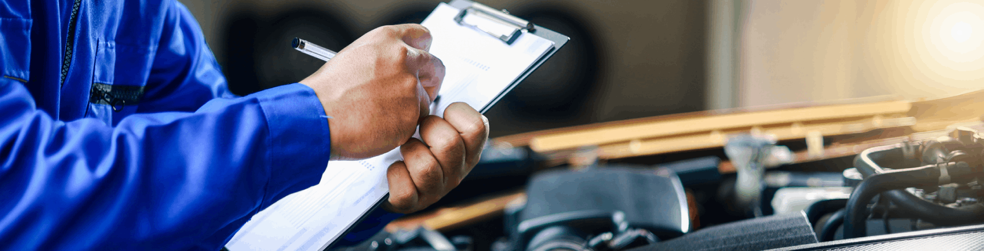 Mechanic with a clipboard and a pen checking under the hood of a vehicle during a pre-purchase inspection.
