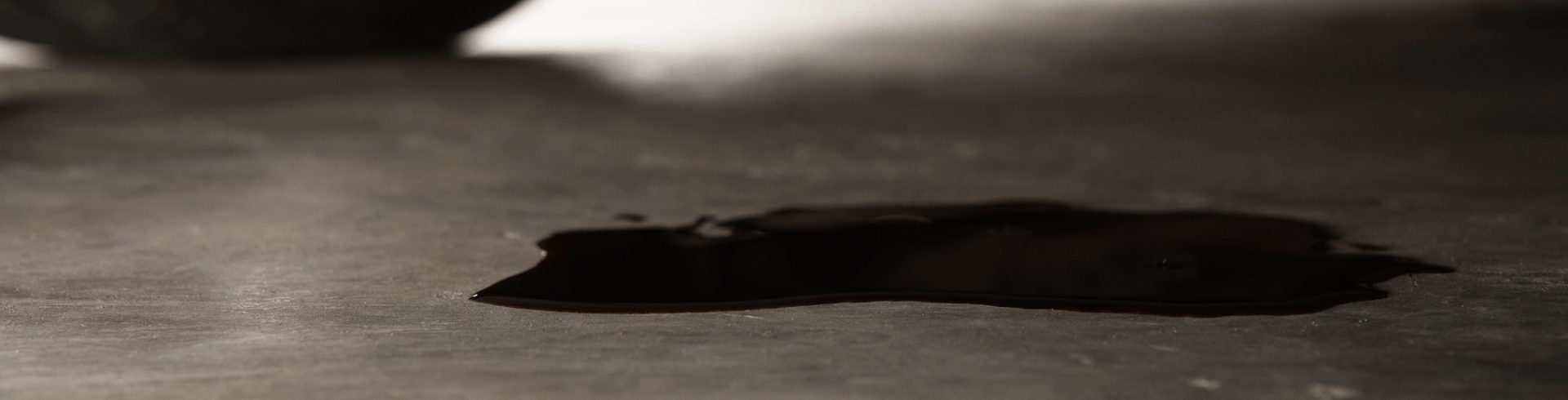 Close-up, a MINI Cooper leaking oil from engine onto the concrete floor.