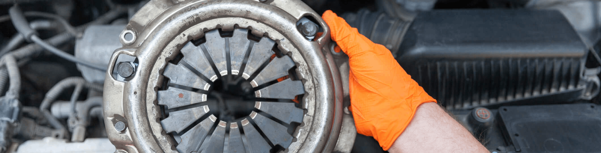Professional mechanic replaces a MINI Cooper’s clutch, holding up the old part.