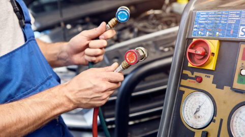 Mechanic holds a set of high-pressure pipes for filling the car's air conditioning system.