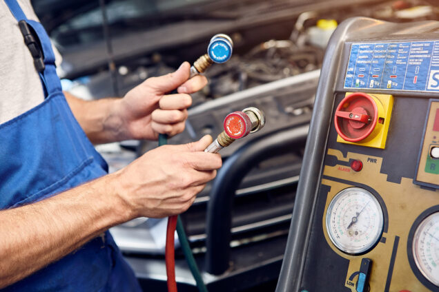 Mechanic holds a set of high-pressure pipes for filling the car's air conditioning system.