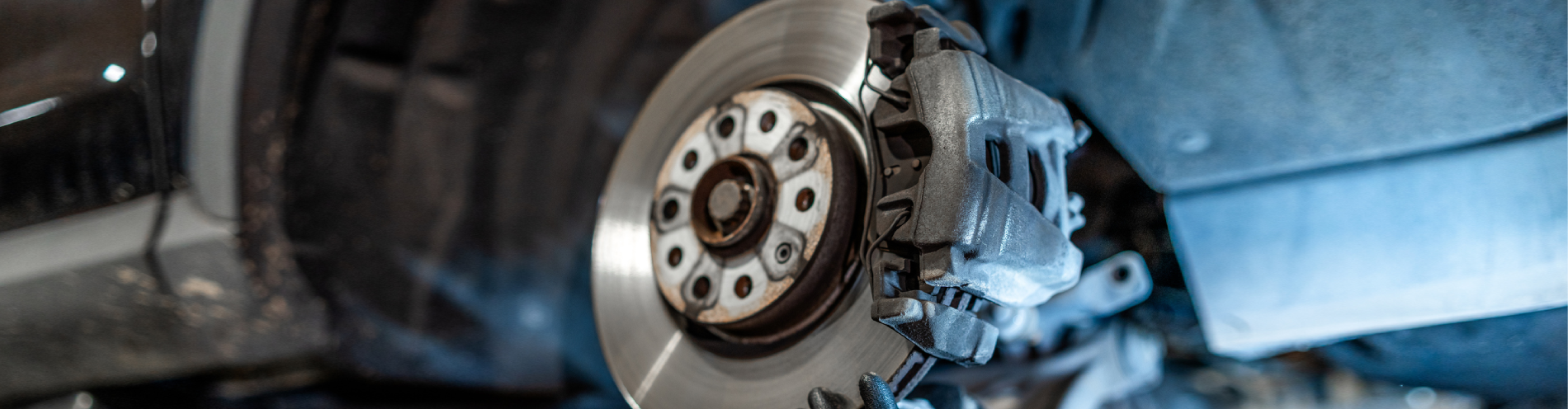 Close up of mechanic's hands wearing gloves, inspecting car brake disc and caliper during maintenance in auto repair shop.