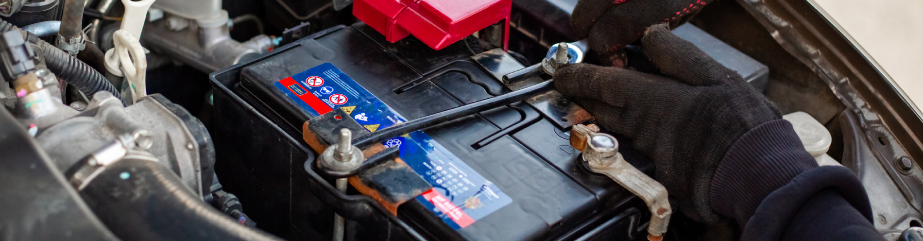 Replacing a car battery. The mechanic installs the battery, securing the battery mounting bracket with a wrench.