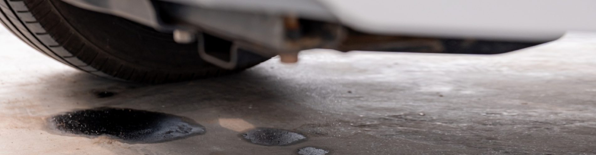 Close-up of oil leaking from a car onto a concrete floor.