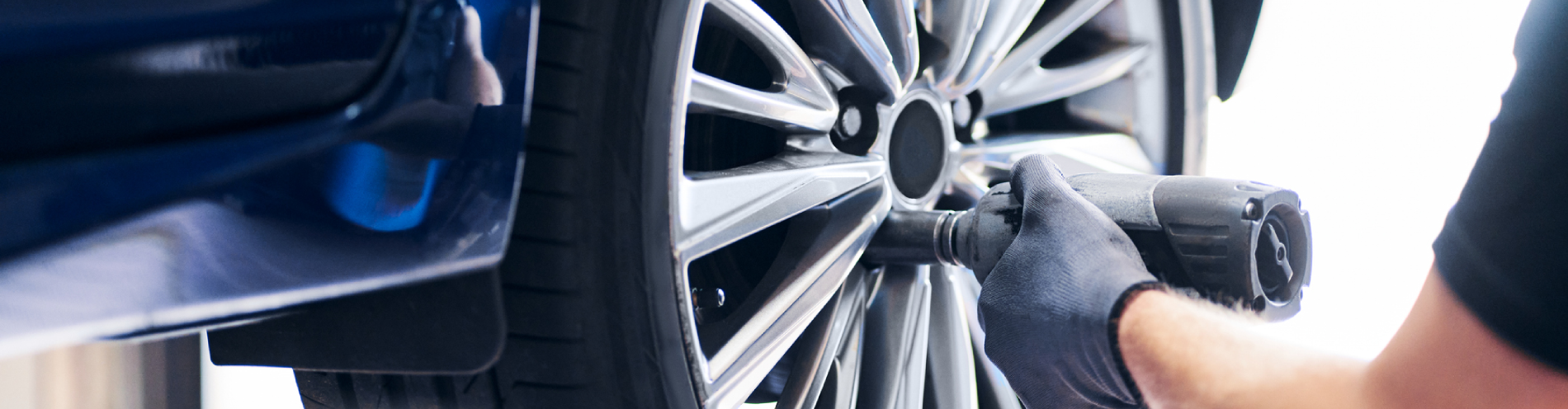 Mechanic changing car wheel in auto service using pneumatic wrench.