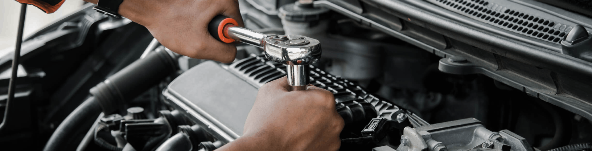 Professional mechanic performing scheduled maintenance. The hood is open and they are using a wrench on the engine.