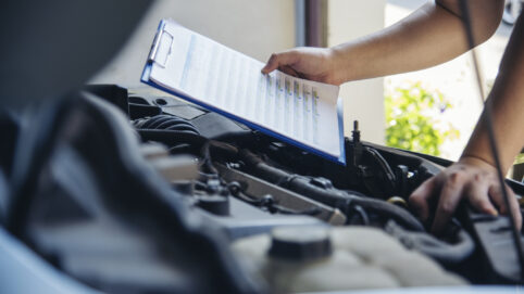 Close up of Woodinville Sports Cars mechanic with a checklist inspecting vehicle engine.