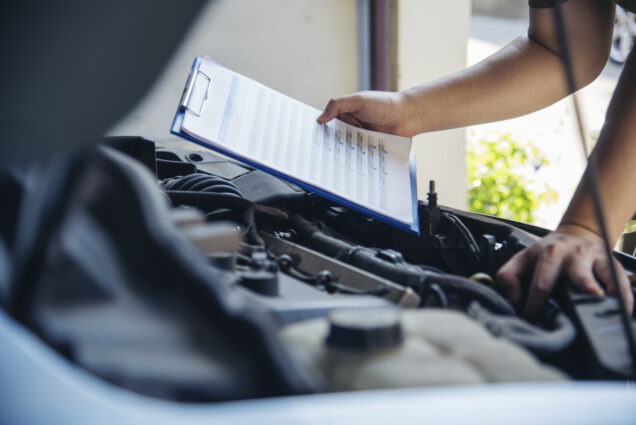 Close up of Woodinville Sports Cars mechanic with a checklist inspecting vehicle engine.