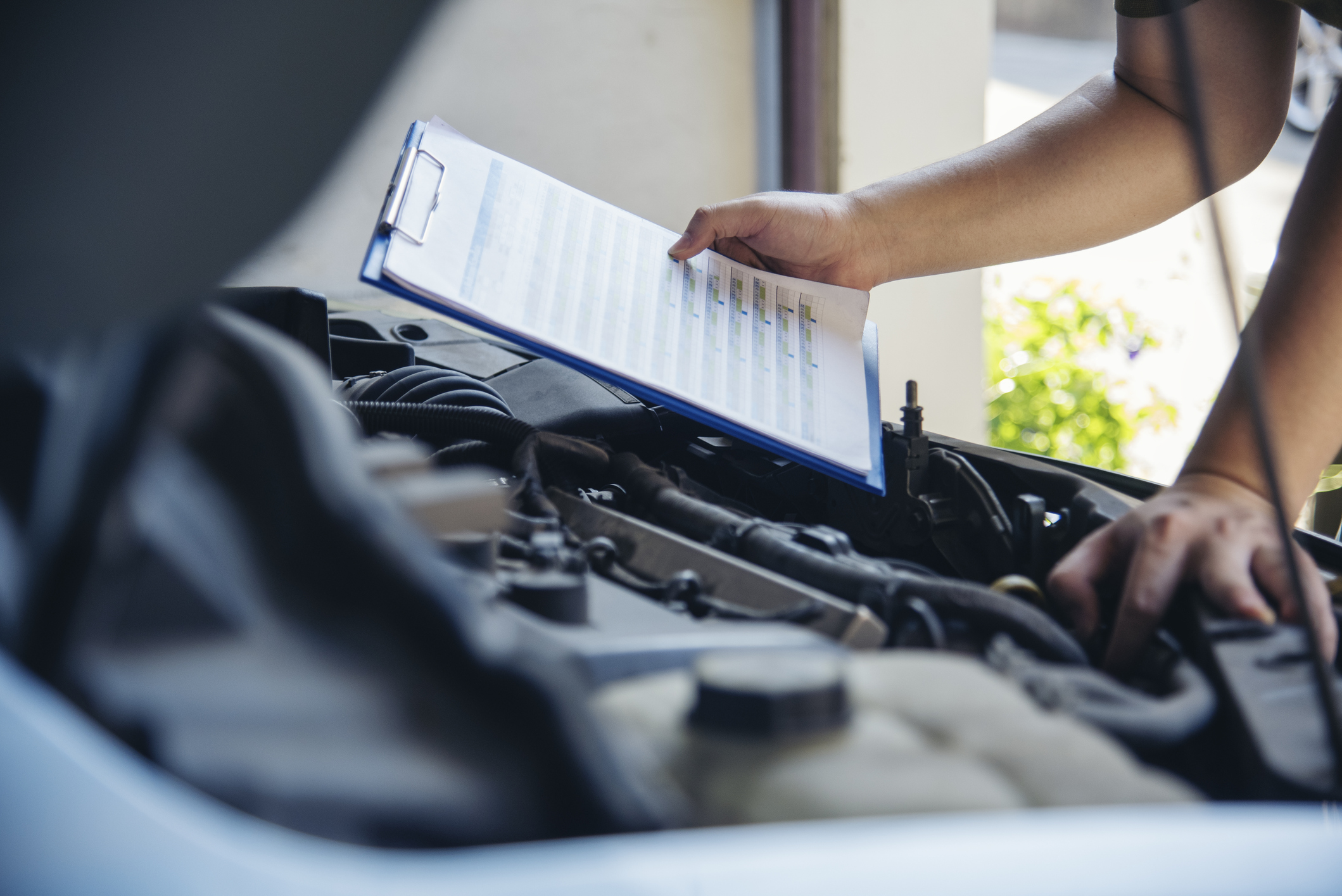 Close up of Woodinville Sports Cars mechanic with a checklist inspecting vehicle engine.